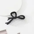 Detailed close-up of matte black bow hair claw clip on a minimalist white display - Black