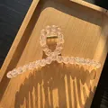 Macro shot of light pink frosted beaded hair claw clip with golden metal spring on wood tray - Transparent Orange