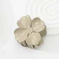Glänzende cremefarbene Blumen-Haarklammer auf einem minimalistischen weißen Sockel - Khaki