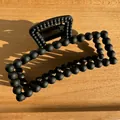 Close-up of black matte bead hair claw clip on a wooden surface with metal spring detail - Black
