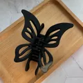 Close-up of matte black hollow butterfly hair claw clip on a wooden display tray - Black