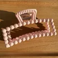 Detail of matte pink rectangular hair claw clip with ball bead texture on light wood - Pink