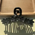Detail of matte black floral hair claw clip on wooden tray with natural sunlight shadow - Black