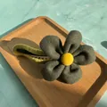 Detailed shot of large plush flower hair clip with yellow center on wood tray - Green