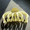 Detalle de pinza de pelo tipo pulpo crema mate sobre madera con sombras artísticas - Blanco Roto
