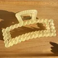 Détail de la pince à cheveux carrée jaune crème mat sur fond en bois clair - Jaune