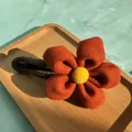 Detail of orange plush flower hair clip with yellow center on a wooden tray - Red
