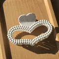 Detail der weißen herzförmigen matten Haarklammer mit Perlenrand auf einem Holztablett - Weiß