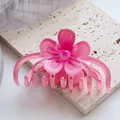 Close-up of a translucent pink flower hair claw clip on a textured stone coaster - Pink