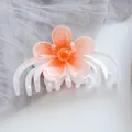 Detailed macro view of a floral hair claw with frosted orange gradient petals and white teeth - White Orange