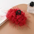 Detail shot of a red ostrich feather hair claw clip next to an elegant perfume bottle - Red