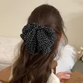 Detalle de un lazo retro con lunares blancos sobre cabello ondulado castaño - Negro
