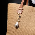 Detail of seashell charm with golden leaf and pearls hanging on a woven straw bag - Monstera Leaf Pearl Conch Style (HWBC766-4)