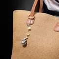 Close-up of ocean shell keychain with pearl and metal flower on a straw bag - Yellow Flower Pearl Conch Style (HWBC766-6)