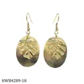 Macro shot of gold Monstera leaf earrings on oval mother of pearl shell with hook - Hollow Monstera Leaf Design (HWB4289-18)