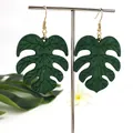 Groene houten monstera blad oorbellen met gouden haken op een zilveren standaard - Donkergroen