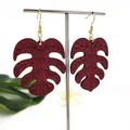 Donkerrode monstera blad houten oorbellen met gouden haken op witte standaard - Donkerrood