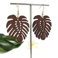 Detail van donkerbruine houten monstera blad oorbellen met gouden haken op standaard - Hol Ontwerp 2 (HWX1514-2) / Donkerbruin