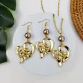 Dettaglio di un set di gioielli cuore dorato e fiore con perle su base in marmo - Marrone scuro