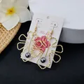 Golden monstera leaf outline earrings with dark pearl drop on Aloha card packaging - Dark Gray Bead Style (HWX693-12)
