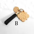 Macro view of gold flower charm with letter B engraving and black suede tassel keychain - Letter B-Gold Tassel