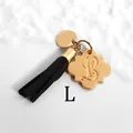 Detailed macro of golden letter L charm with black tassel on faceted stone bracelet - Letter L-Gold Tassel
