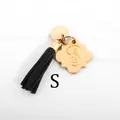 Close-up of golden letter S pendant with black tassel on white marble background - Letter S-Gold Tassel