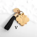 Detailed view of golden flower charm with letter V and black suede tassel on marble background - Letter V-Gold Tassel