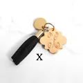 Detail of golden petal charm with letter X and black suede tassel on white marble - Letter X-Gold Tassel