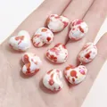 Handheld view of white heart-shaped ceramic beads with red ink splatter for DIY jewelry - 14x16mm (4 Pieces/Pack) / Red