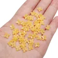 Handheld view of yellow four-petal resin flower beads for DIY jewelry making - 7mm (20 Pieces/Pack) / Dark Yellow