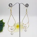 Close-up of golden teardrop earrings with elegant white pearls on a minimalist stand - White