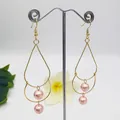 Detailed shot of double-layered teardrop pearl earrings with gold tassels on a stand - Pink