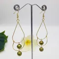 Detail of gold teardrop earrings featuring olive green pearls on a minimal display - Olive