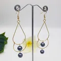 Detailed macro view of gold pear-shaped drop earrings with dual grey pearls on a display - Dark Grey Style