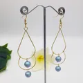 Detailed close-up of double-layer gold teardrop earrings with iridescent blue pearls - Magic Blue