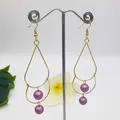 Detailed view of long water drop earrings with purple pearls on a golden wire frame - Purple
