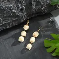 Close-up of handmade white tulip flower petal earrings on a black stone background - Cream White (HWX2727-6)