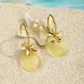 Gelbe Meeresglas-Ohrringe mit goldenem Blumenverschluss auf weißem Sand im Detail - Yellow Style (HWG018-5)