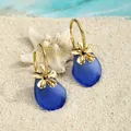 Detail von blauen Meeresglas-Ohrringen mit goldenen Blumen auf weißem Strandsand - Dark Blue Style (HWG018-6)