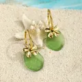 Detailansicht der Goldblumen-Ohrringe mit grünem Seeglas-Anhänger auf weißem Sand und Seestern - Forest Green Style (HWG018-9)