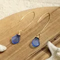 Detailansicht handgefertigter Seeglas-Ohrringe mit Golddrahtwicklung auf Sand und Muscheln - Blau (HWG016-9)