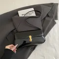 Glossy black patent leather baguette bag with a gold lock on a grey blazer background - Black