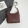 Dark brown pebble leather shoulder bag with gold logo in a premium lifestyle setting - Brown