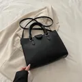 Elegant black lychee textured tote bag with gold hardware on beige blazer background - Black