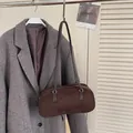 Retro coffee brown suede baguette bag with silver zipper next to a wool coat - Brown