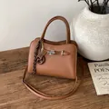 Brown faux leather crossbody bag with silver twist lock and decorative charms on a wood table - Brown with Pendant