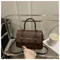 Detalle de bolso de cuero marrón oscuro con correas decorativas en soporte transparente - Café