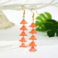 Detail view of orange resin lily flower drop earrings hanging on a white wooden branch - Long