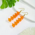 Orange resin flower drop earrings with golden hooks on white textured stone background - Long